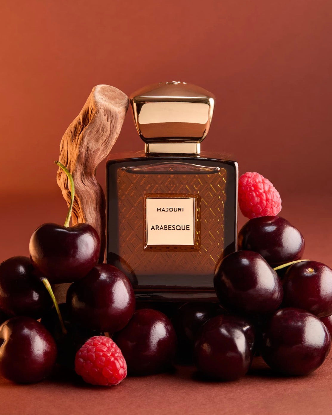 Majouri Arabesque parfumflacon met gouden dop, omringd door donkere kersen, frambozen en hout.