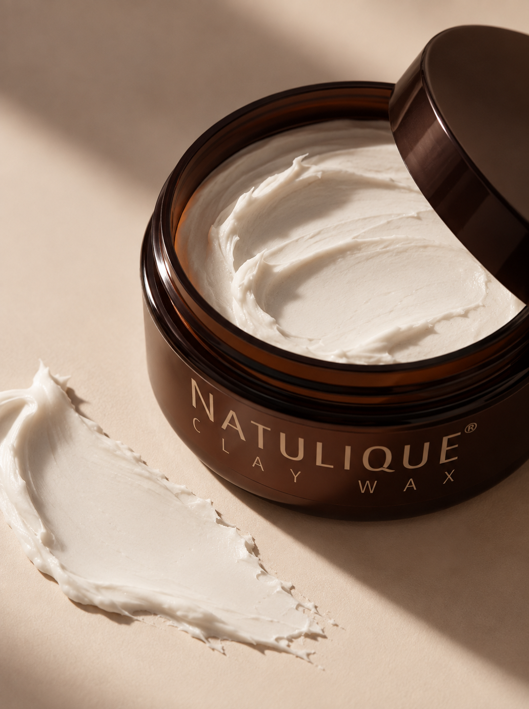 
                  
                    NATULIQUE Clay Wax in een open pot met wax op de ondergrond
                  
                